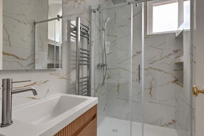 Ein Badezimmer mit einem weißen Waschbecken, einer Duschkabine aus Glas und Wänden mit Marmoroptik.