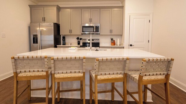 Una cocina con una isla central, tres taburetes de bar y electrodomésticos modernos.