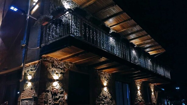 A building with a balcony, stone pillars, and outdoor lighting.