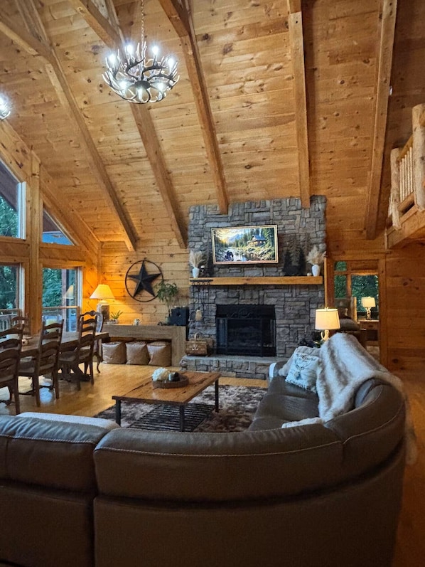 A cozy log cabin interior with a stone fireplace, a chandelier, and a dining area. - Perfect Mountain Getaway! Southern Bear Cabin offers IT ALL! (Jasper)