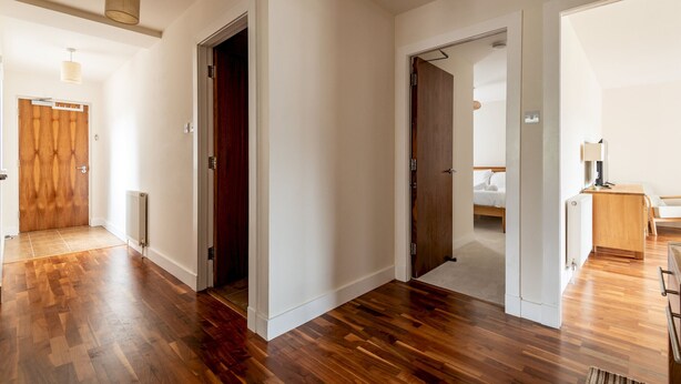 Um quarto espaçoso com assoalho de madeira, porta de madeira e cama com roupa de cama branca.