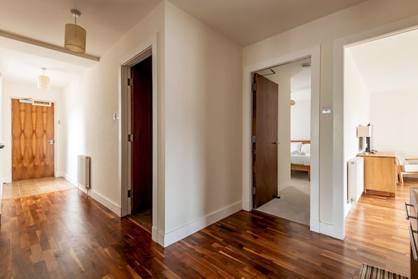 A spacious room with hardwood flooring, a wooden door, and a bed with white bedding. - Southfield Apartments (No 15) | St Andrews (St Andrews)