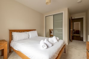 A neatly made bed with white linens, a wooden headboard, and two rolled towels on the bed. - Southfield Apartments (No 15) | St Andrews (St Andrews)