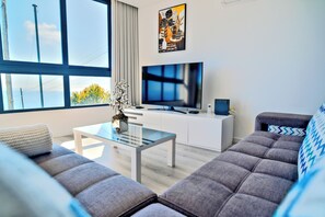 Ein modernes Wohnzimmer mit einer Couch, einem Glastisch, einem Flachbildfernseher und einer Zimmerpflanze.