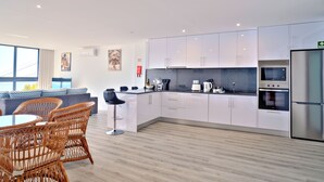 Eine moderne Küche mit weißen Schränken, einem Edelstahl-Kühlschrank und einem Essbereich mit Korbstühlen und einem runden Tisch.