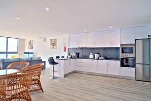 Eine moderne Küche mit weißen Schränken, einem Edelstahl-Kühlschrank und einem Essbereich mit Korbstühlen und einem runden Tisch.