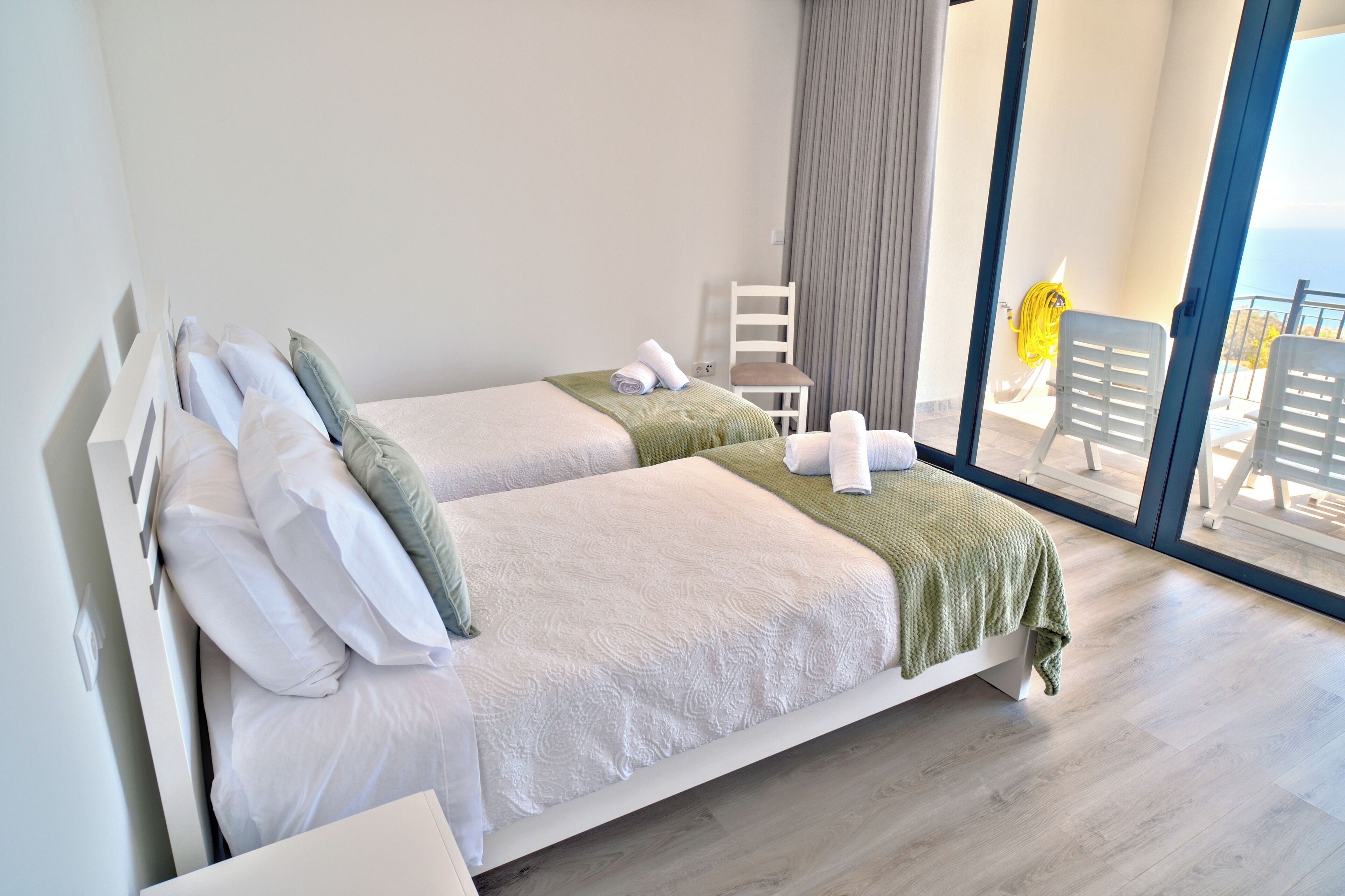 A hotel room with two beds, a chair, a balcony with a view, and a window.