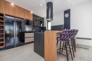 Een moderne keuken met een centraal eiland, barkrukken en een decoratieve klok aan de muur.