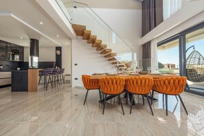 A modern kitchen with a central island, a dining area with orange upholstered chairs, and a staircase leading to an upper level. - Villa Niksun (Bibinje)