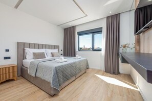 A modern hotel room with a bed, a bedside table, a window with curtains, and a view of the city. - Villa Niksun (Bibinje)