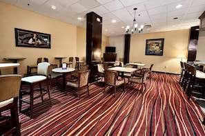 A hotel lobby with striped carpet, multiple dining tables and chairs, a television, and artwork on the walls.