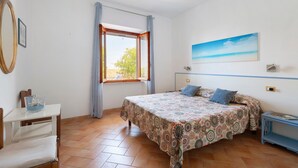 Un dormitorio con cama, ventana con cortinas, un cuadro en la pared y una mesita de noche con lámpara.