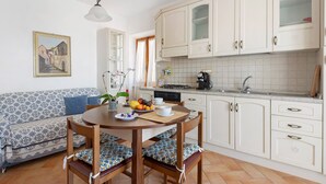 Una cocina con armarios blancos, una mesa de comedor con sillas, un sofá y un cuadro en la pared.