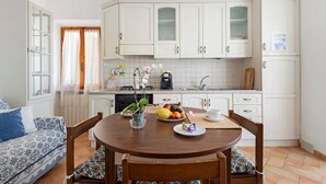 Una cocina con armarios blancos, una mesa de comedor con sillas y un frutero sobre la mesa.
