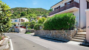 Una calle residencial con casas, un muro de piedra y una colina al fondo.