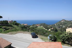 Una carretera costanera amb un cotxe estacionat, cases i una vista clara del mar.
