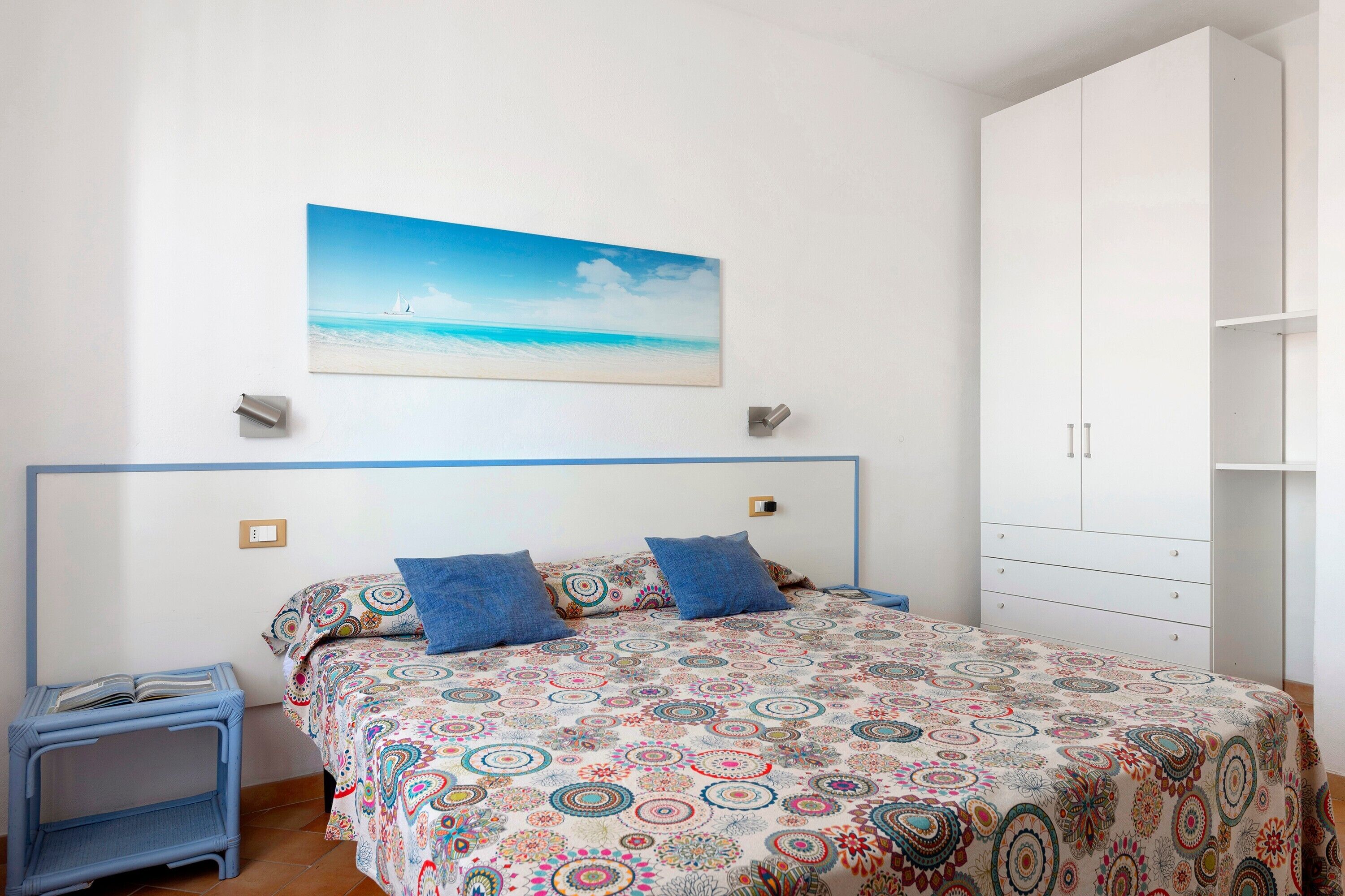 Una camera da letto con un letto, un comodino, un armadio e un quadro raffigurante una spiaggia.