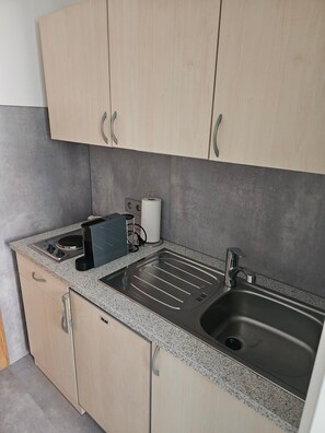 Cozinha com armários de madeira clara, bancada de granito, pia de aço inoxidável, cafeteira e porta-papel toalha.