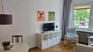 A modern living room with a TV, white cabinets, a dining table, and a chair.