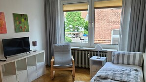A modern hotel room with a bed, a chair, a TV, a small table, and a window with a view of the outside.