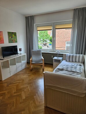 Ein modernes Hotelzimmer mit Bett, Sessel, Fernseher, kleinem Tisch und Fenster mit Aussicht.