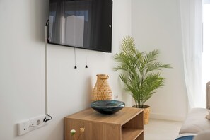 Ein modernes Wohnzimmer mit einem an der Wand montierten Flachbildfernseher, einem Holztisch mit einer Schale, einer Korbvase und einem Blumentopf.