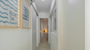 A narrow hallway with a framed picture on the left, a small table with a plant at the end, and a window on the right. - 2-bedroom Apartment in Guargacho, Tenerife (Arona)