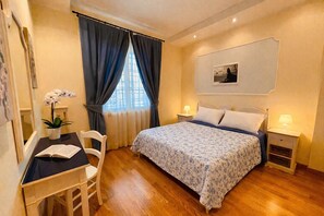 A bedroom with a bed, bedside tables, a desk, a chair, and a window with curtains. - Giardino dei colori - App. 307 by Theater Home, with balcony and pool (Toscolano-Maderno)