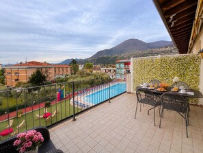 A balcony with a view of a swimming pool, a dining table with chairs, and a decorative wall. - Giardino dei colori - App. 307 by Theater Home, with balcony and pool (Toscolano-Maderno)