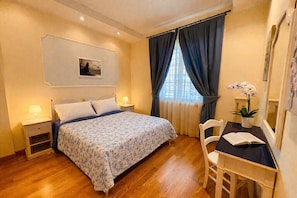 Ein Schlafzimmer mit einem Bett, Nachttischen, einem Schreibtisch mit Stuhl, einer Topfpflanze und einem Fenster mit Vorhängen.