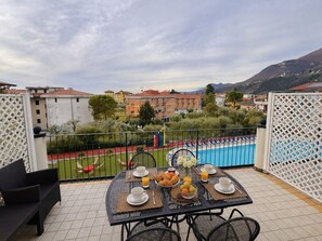 Una terraza con una mesa dispuesta para el desayuno, una piscina y edificios al fondo.