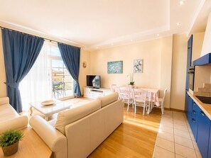 Ein modernes Wohnzimmer mit einer Couch, einem Esstisch mit Stühlen, einem Fernseher und einer Küchenzeile mit Schränken.