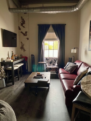 A living room with a sofa, a coffee table, a TV, a window with curtains, and a lamp. - Downtown 2 bedroom apartment. 20 minute walk to Sanford Stadium (Athens)