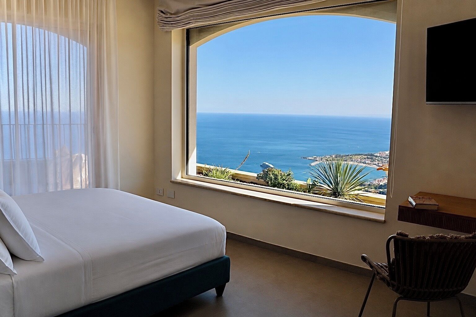 A hotel room with a large bed, a view of the sea, and a chair.