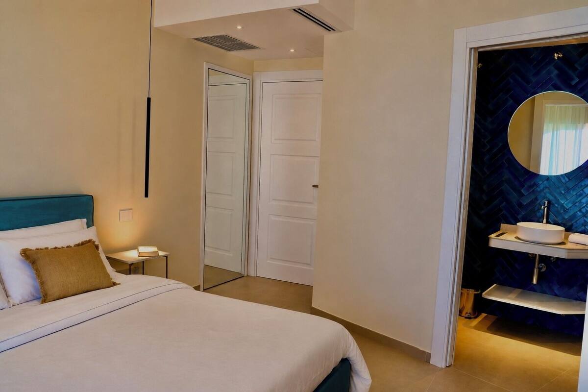 A hotel room with a bed, bedside table, and a bathroom with a mirror and sink.