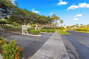 A hotel entrance with a gated driveway, palm trees, and a clear sky. - Includes Beach Gear!  E305 Vista Waikoloa (Waikoloa)