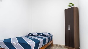 Una cama individual con una colcha estampada, un armario de madera y un suelo con motivo de espiga.