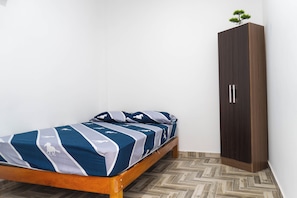 Una cama individual con una colcha estampada, un armario de madera y un suelo con motivo de espiga.