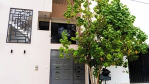 Un edificio moderno de dos pisos con fachada geométrica, una escalera visible y un árbol en primer plano.
