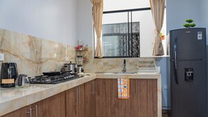 Una cocina moderna con encimeras de mármol, armarios de madera, un refrigerador negro y una ventana con cortinas.