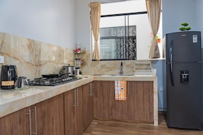 A modern kitchen with marble countertops, wooden cabinets, a black refrigerator, and a window with curtains.