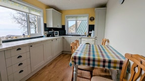 A kitchen with white cabinets, a microwave, a sink, and a table with a checkered tablecloth. - 2-bed Country Cottage, Sleeps 5 & Pet Friendly (Helmsdale)