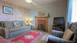 A living room with a sofa, armchair, fireplace, television, and a patterned rug. - 2-bed Country Cottage, Sleeps 5 & Pet Friendly (Helmsdale)