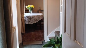 A hallway leading to a dining area with a table and chairs, a potted plant, and a door.