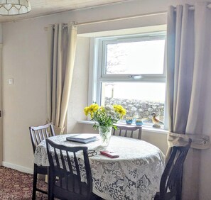 A dining area with a table, chairs, a vase with flowers, and a window with curtains. - 2-bed Country Cottage, Sleeps 5 & Pet Friendly (Helmsdale)