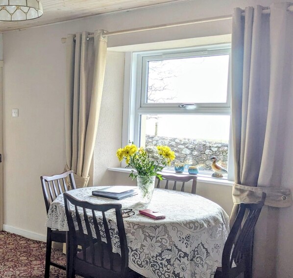 Un coin repas comprenant une table, des chaises, un vase avec des fleurs et une fenêtre avec des rideaux.