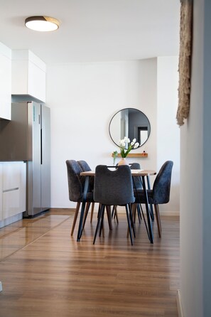 A modern kitchen with a built-in refrigerator, a dining table with chairs, and a round mirror on the wall. - Modern Family Suite in Prizren (Prizren)