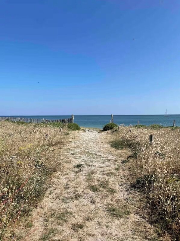 A sandy path leading to a beach with a wooden fence on one side and a sailboat in the water. - Beach House / Rhuys Peninsula (Sarzeau)