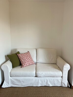 A white leather sofa with two pillows, one green and one with a red pattern, against a plain wall. - Beach House / Rhuys Peninsula (Sarzeau)