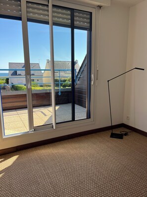 Ein Zimmer mit einem großen Schiebeglastür, die auf einen Balkon führt, einer Stehlampe und einem Teppichboden.